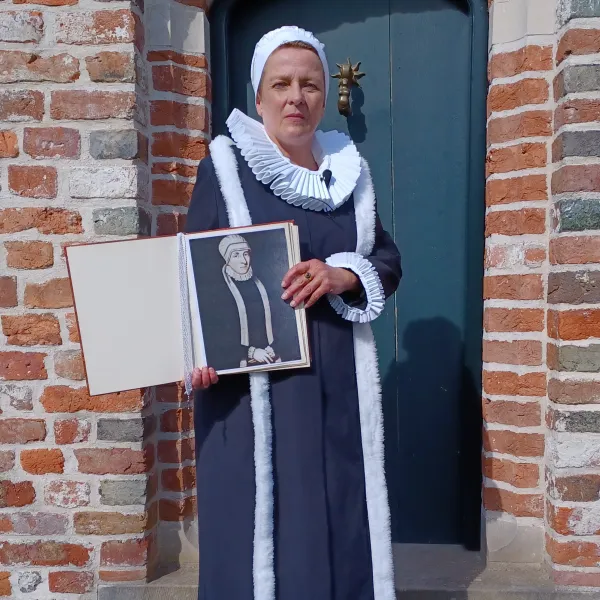 Frau in historischer Tracht hält ein Porträt von Gräfin Anna von Ostfriesland vor Backsteinmauer.