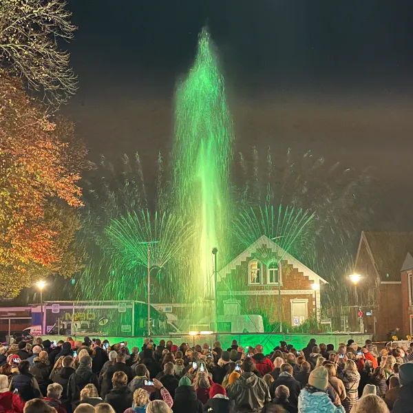Menschenmenge beobachtet abends eine grün beleuchtete Wasser- und Lichtshow vor historischen Gebäuden