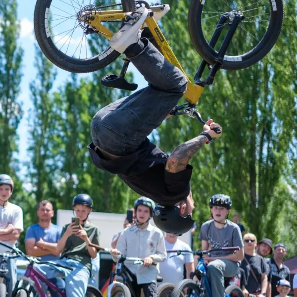BMX-Fahrer mit Helm macht einen Rückwärtssalto vor Publikum auf der Pumptrack-Anlage.