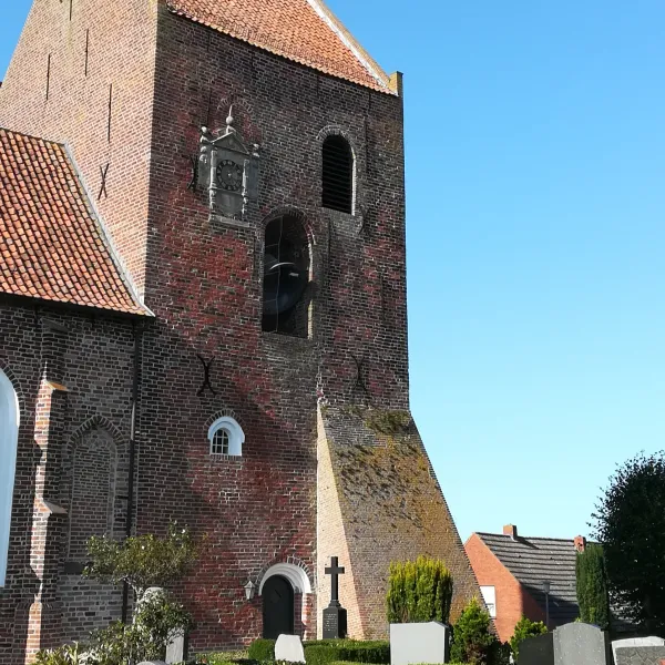 Backsteinkirche mit hohem Turm und rotem Ziegeldach vor blauem Himmel, umgeben von Grabsteinen.