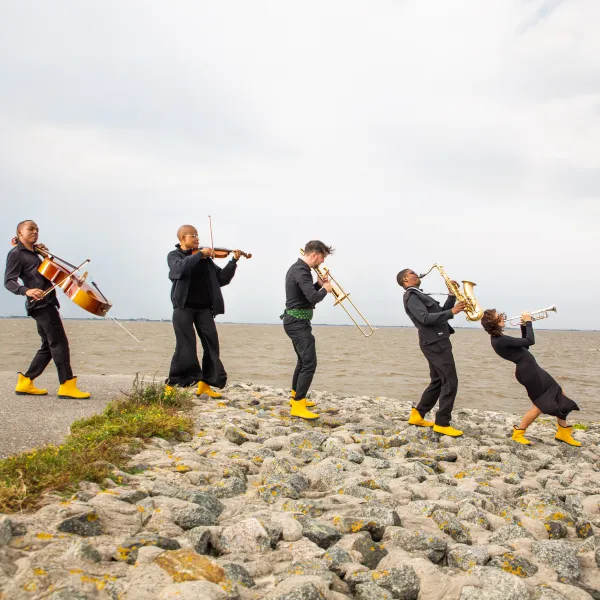 Musiker und Musikerinnen mit gelben Gummistiefel und Musikinstrumenten am Strand