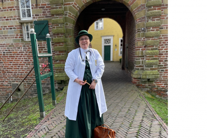 Frau in historischer Arztkleidung mit Stethoskop und Tasche vor dem Tor der Manningaburg Pewsum