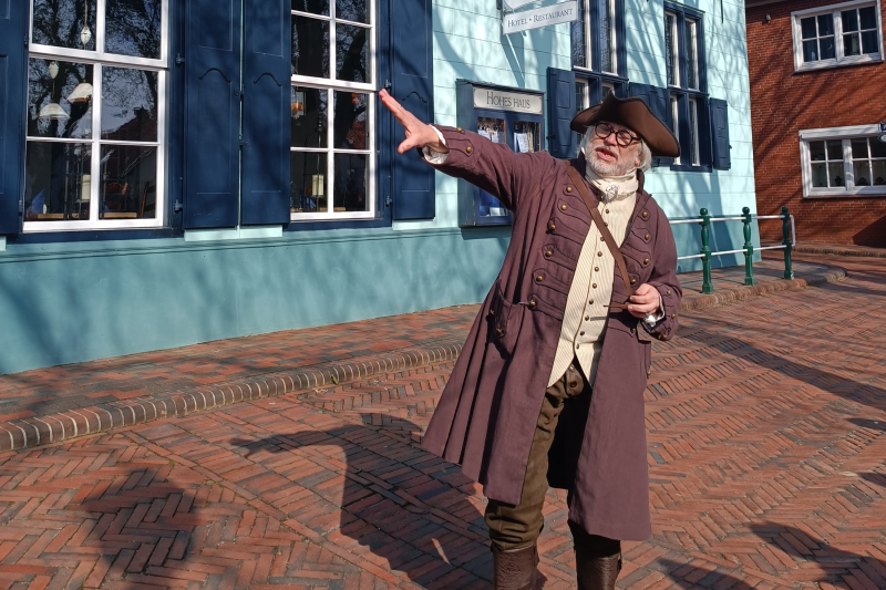 Mann in historischer Kleidung als Hafenmeister Quirinus steht vor dem hellblauen Hotel Hohes Haus.