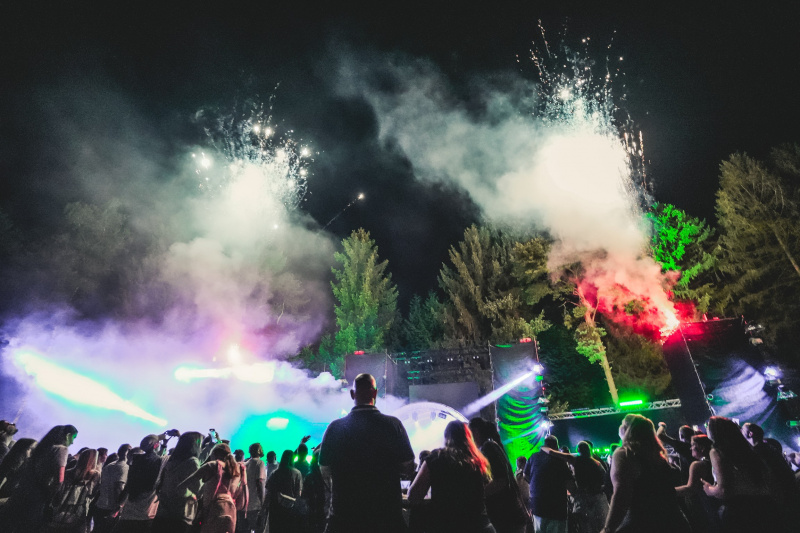 Festivalpublikum feiert nachts vor einer beleuchteten Open-Air-Bühne mit Nebel und Lichteffekten.