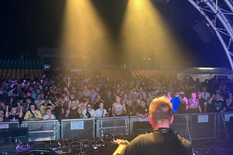 Ein DJ am Mischpult blickt nachts auf die feiernde Menge beim Planet Future Festival.