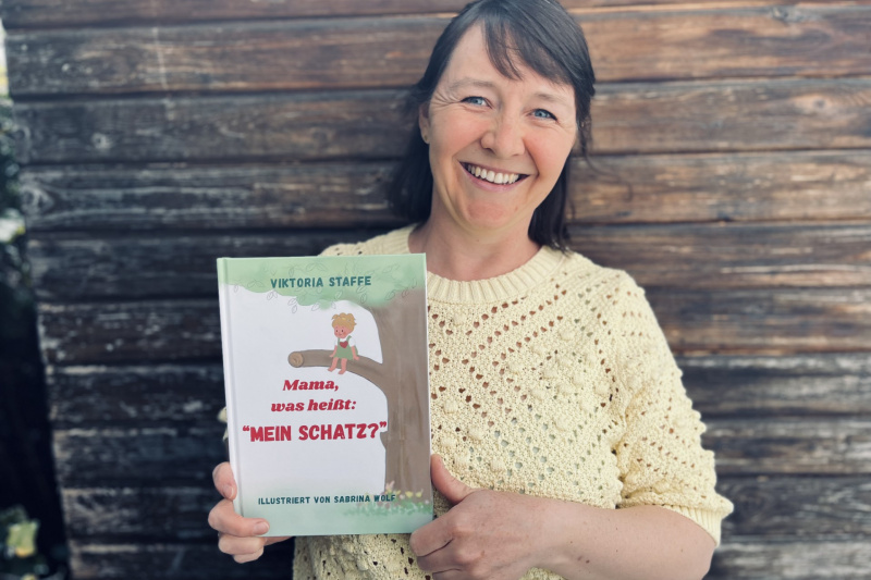 Autorin Viktoria Staffe lächelt und präsentiert ihr Kinderbuch Mama, was heißt mein Schatz.