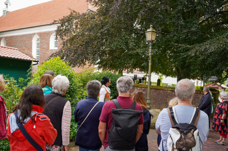 Kostümführerin erklärt einer Gruppe die Geschichte an der Kirche in Greetsiel.