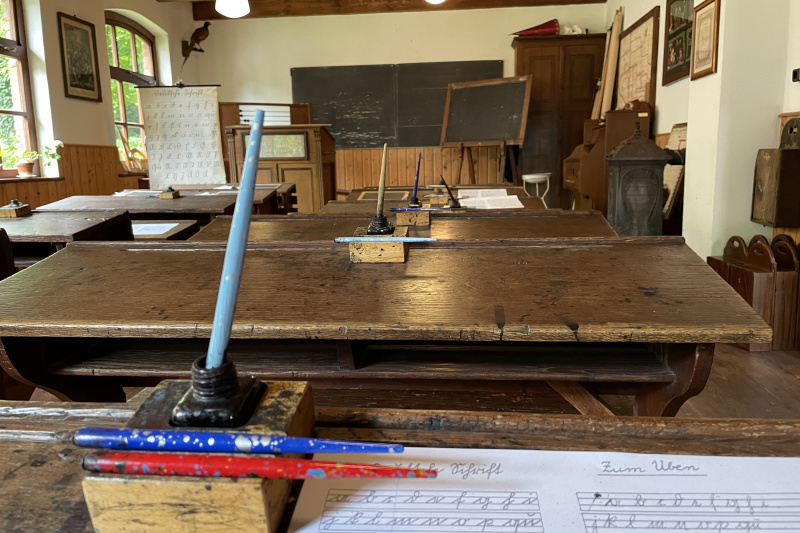 Symbolbild altes Klassenzimmer mit alten Schreibheften, alte Füller, Tintenfass und Kreidetafel