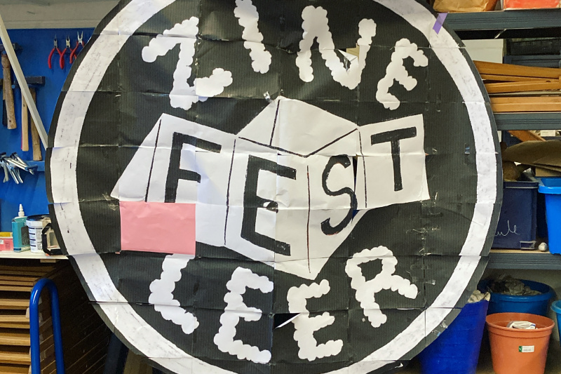 auf diversen DinA4-Blättern ausgedrucktes Logo des Zine Fest Leer, aufgehängt an einem Werkstattregal
