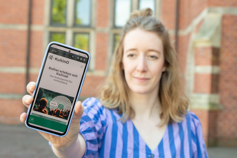 Frau hält ein Smartphone mit der geöffneten KultinO-Website in die Kamera