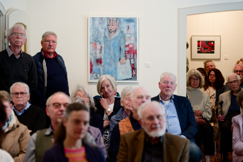 Aufmerksames Publikum, im Hintergrund das Bild „Auf der Flucht“ 