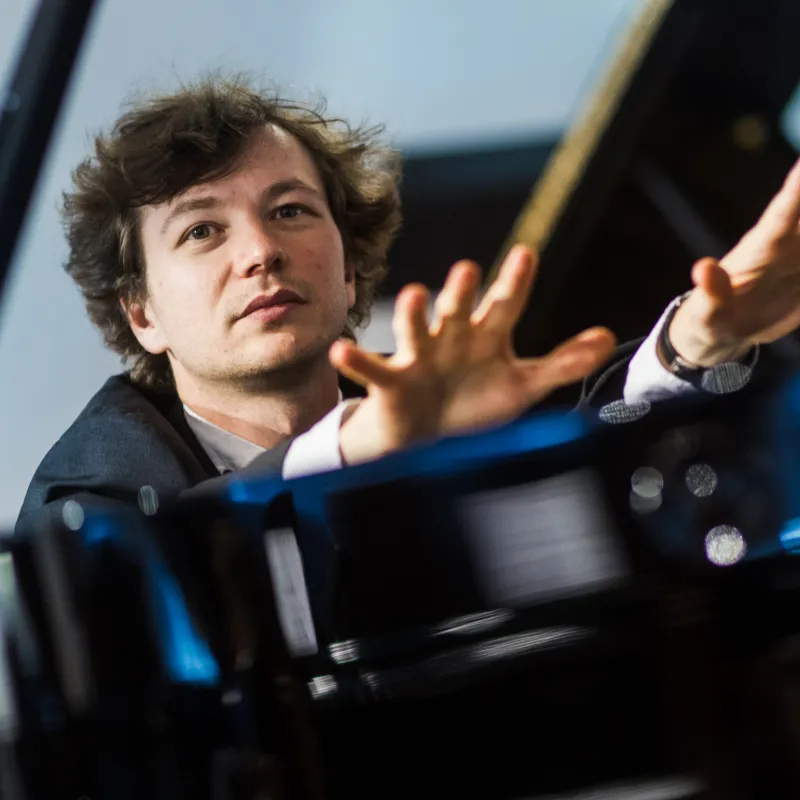 Pianist Mikhail Mordvinov am Flügel mit erhobenen Händen.