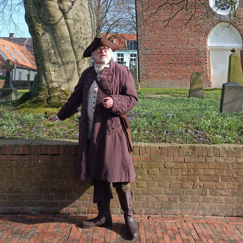 Hafenmeister Quirinus im historischen Gewand mit Dreispitz vor der alten Backsteinkirche.