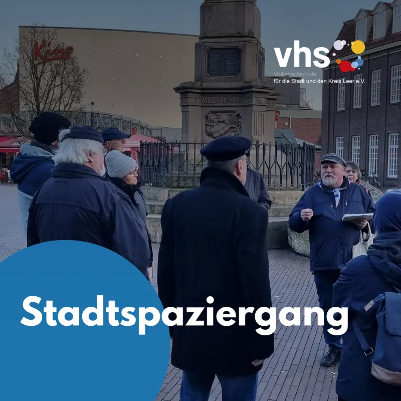Eine Gruppe von Teilnehmenden hört während eines geführten Stadtspaziergangs in Leer einem Stadtführer vor einem Denkmal aufmerksam zu. 