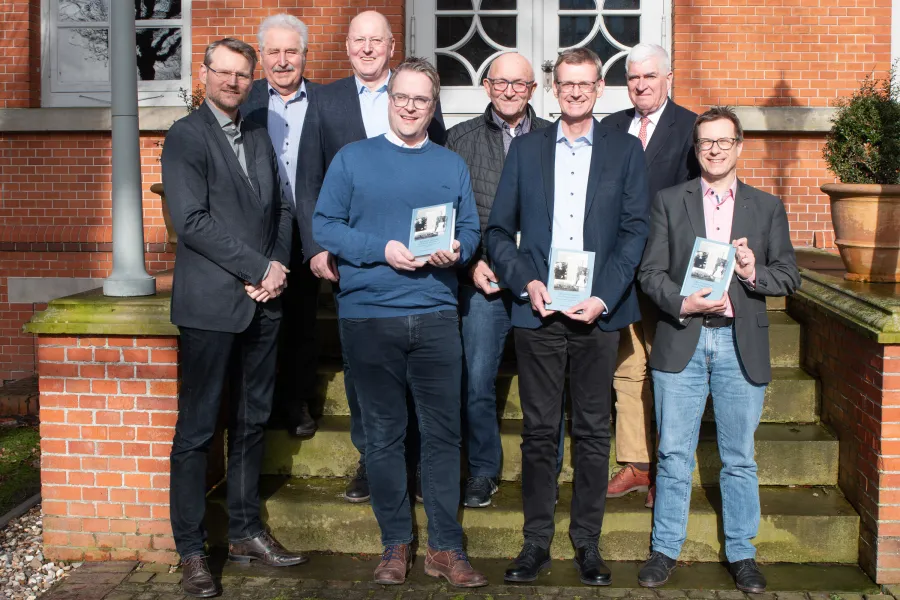 Acht Männer auf einer kleinen Steintreppe halten Bücher in den Händen