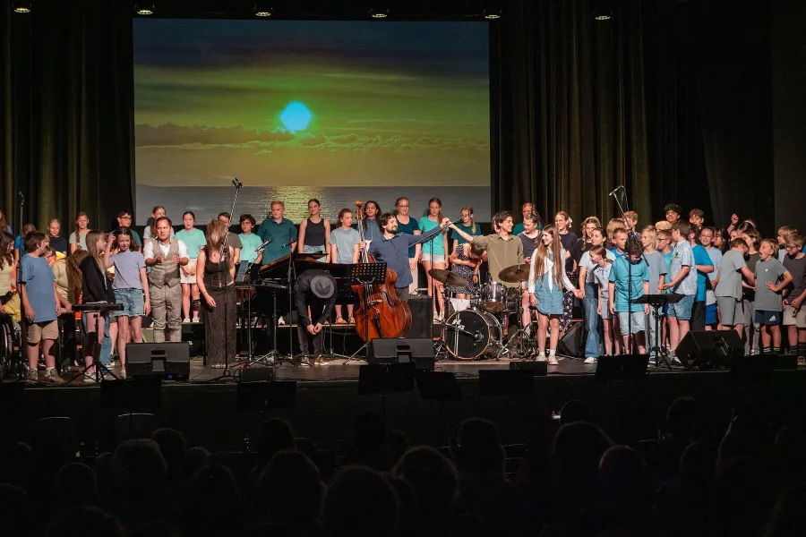 100 Schülerinnen und Schüler mit Band und Sängerin Ella Burghardt samt Flutlichter-Bühnenbild und Publikum