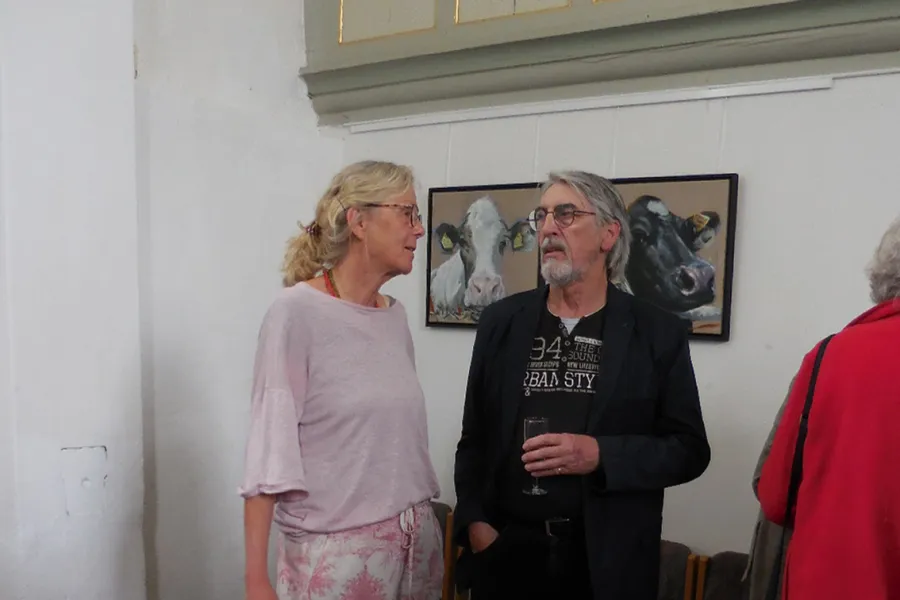 Laudatorin Dr. Annette Kanzenbach und Künstler Hartmut Bleß vor Kuh-Bildern von Ulrich Schnelle